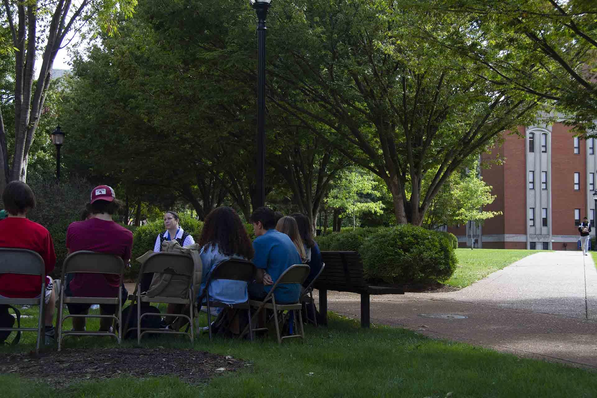 Students sitting outside under a bower of green leaves.