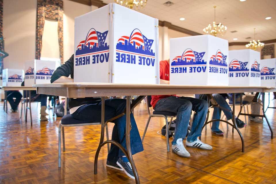 Students vote behind small barriers that read Vote Here at tables in the Saint Louis Room.